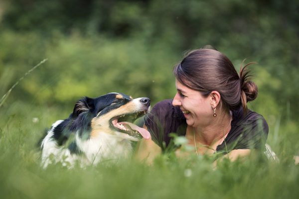 Tierkommunikatorin liegt in Wiese mit Australian Shepherd Hund