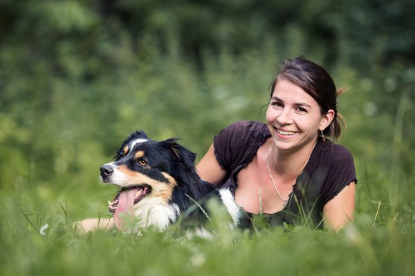 Susanne Eggers liegt in der Wiese mit Australian Shepherd Hündin Amy